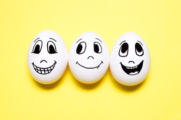 Three eggs with drawn smiling cartoon faces on yellow background