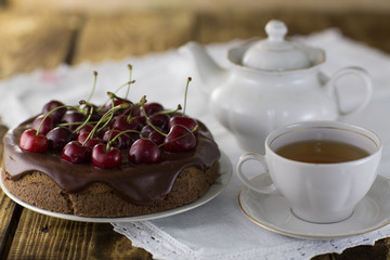 A cherry pie, with fresh cherries a cup of tea and a kettle.  Home made