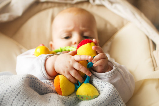 a small child lies and plays with a toy. A newborn baby in a deckchair with a toy in hand