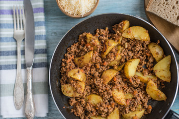 Fried ground beef and potato wedges in a frying pan, close-up - a rustic dish