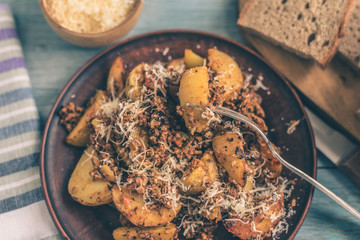 Fried potato wedges with bolognese sauce and parmesan cheese in a clay plate on a rustic wooden background - concept of natural food