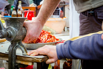 People are mincing meat for handmade sausages at outdoor kitchen
