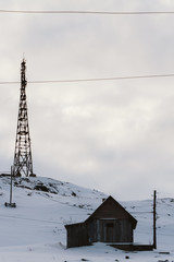 High radio tower in winter near an old wooden house on a high hill