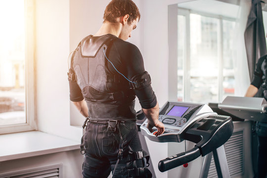 ems training. Fit Man wearing black electromiostimulation suit preparing for running on treadmill near window