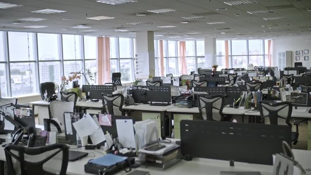 Dolly shot of big empty office with large windows and employees’ things on tables, shot in daytime