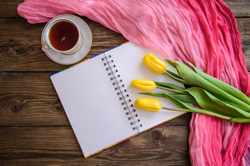 Romantic picture with notepad, tulips and a cup of tea on wooden background
