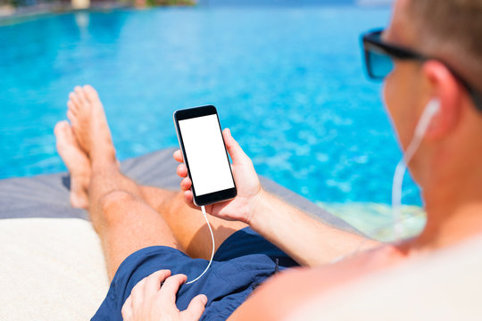 Man listening to music and holding mobile phone in hand by the pool.