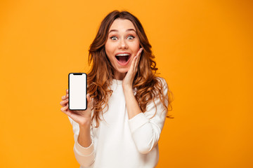 Shocked brunette woman in sweater showing blank smartphone screen