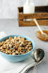 Homemade granola in a blue bowl on a linen napkin with a bottle of milk and honey. Food Photography of a healthy morning breakfast.