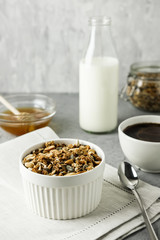 Homemade granola in a blue bowl on a linen napkin with a bottle of milk, cup of coffee and honey. Food Photography of a healthy morning breakfast.