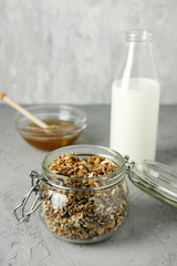 Homemade granola in a glass jar on the concrete background and a bottle of milk and honey. Useful breakfast.