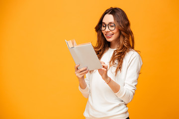 Smiling brunette woman in sweater and eyeglasses reading book