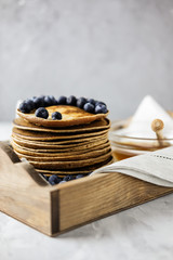 Homemade Chocolate Pancake with blueberries in a wooden tray on the linen napkin with honey. Food photography of a healthy morning breakfast.