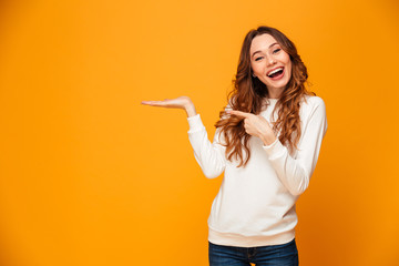 Pleased brunette woman in sweater holding copyspace on the palm