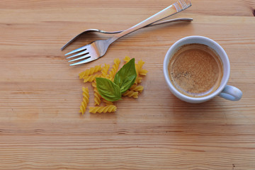 Raw pasta, forks, fresh basil and cup of coffee at wooden background/ conceptual image of dieting