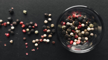 Glass with assorted peppercorns on black background