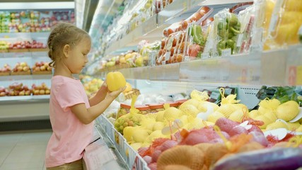 Little cute child girl choosing vegetables in grocery store