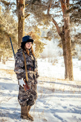 Fototapeta premium Portrait of a beautiful young girl while hunting in a winter pine forest, with a gun