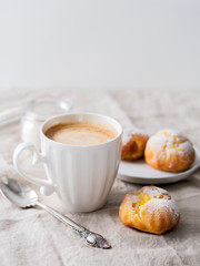 Cakes profiteroles on white plate with cup of coffee.