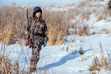 female hunter in camouflage clothes ready to hunt, holding gun and walking in forest. hunting and...