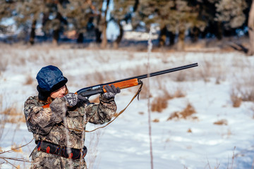 female hunter in camouflage clothes ready to hunt, holding gun and walking in forest. hunting and people concept