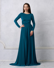 Young woman with long brunette hair dressed in elegant evening teal maxi dress with long sleeves...