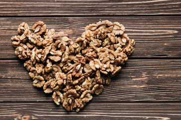 Obraz na płótnie Canvas Heart shaped pile of shelled walnuts on wooden background, healthy eating concept