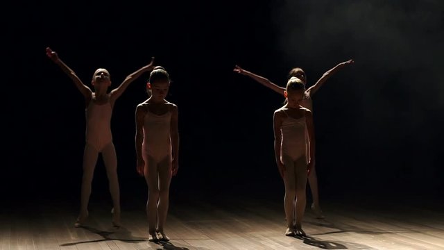 Four little girls in beige swimwear, pantyhose and ballet dancing on stage on a black background, slow motion.