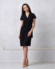 Attractive woman with long brunette hair dressed in fashionable black wrap around midi dress with...