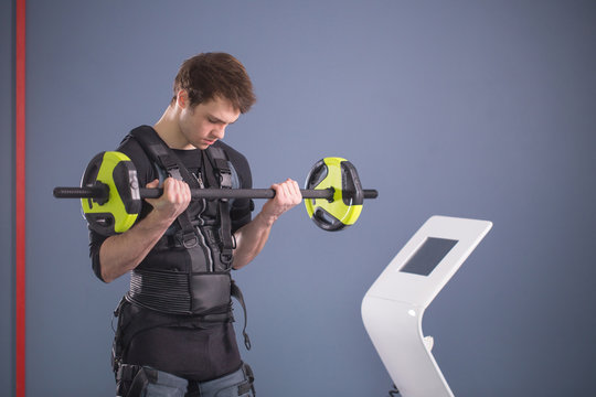 Fit Man wearing black electrostimulation suit lifting barbell closeup, power pose