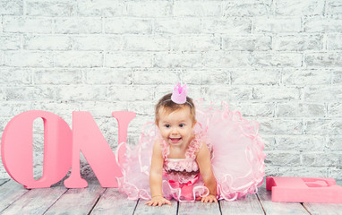 Beautiful and cute girl in a pink dress with the letters one on her first birthday. Emotional girl.