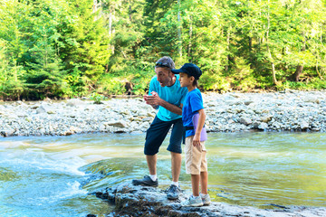 Travelers - father and son are standing on the shore of mountain river