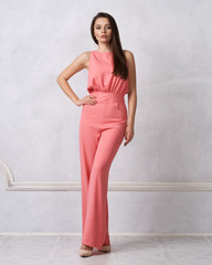 Charming female model with long brunette hair wearing fashionable sleeveless pink jumpsuit and...