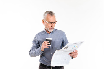 Old concentrated man holding coffee and reading newspaper isolated