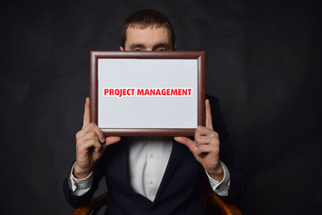 In the hands of a businessman a frame with the inscription:PROJECT MANAGEMENT