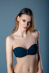 Fototapeta premium Portrait of beautiful charming young woman with long hair in black bra over blue grey background