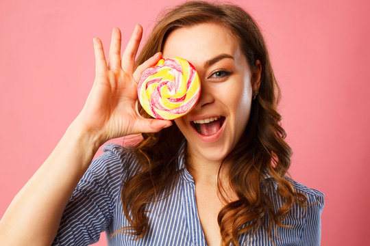 Portrait of a happy pretty girl holding sweet candy over pink background