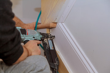 Carpenter brad using nail gun to Moulding trim, with the warning label that all power tools
