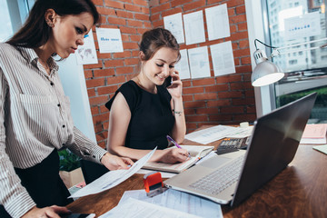 Busy female top manager talking on the phone while her assistant showing her financial statistics