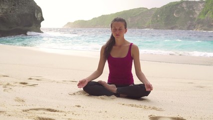 Fototapeta na wymiar Meditating in lotus position, doing yoga exercises in morning on beach