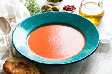 tomato soup in green dish with bread on white wooden background