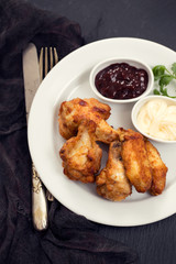 fried chicken with sauces on white plate on black background
