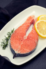 raw salmon with lemon on white dish on black background