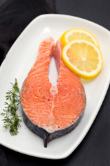 raw salmon with lemon on white dish on black background