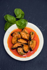 mussels in sauce on white dish on black background