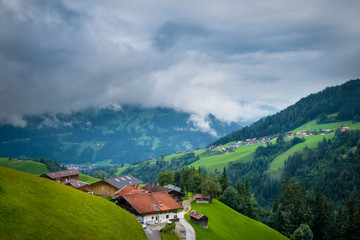 Fototapeta na wymiar Scenic landscape with traditional buildings in village in Alps on the background of nature with green forest, grass and hills. Dramatic clouds