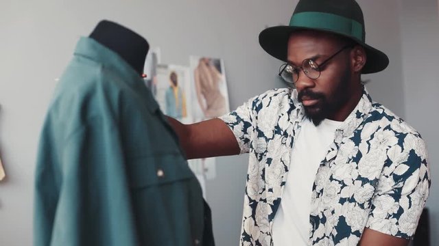 Attractive designer in nerdy glasses crafts new collection, takes sleeves measurements with measuring tape, notes them into his notepad. Comfortable office. Creative mood, inspiration. Slow motion