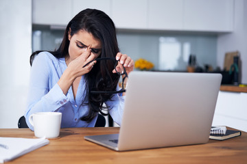 Woman with headache sitting in front of laptop at home