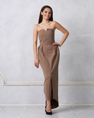 Beautiful brunette female model dressed in strapless taupe brown formal dress posing in studio....