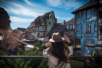 Young unrecognizable woman is standing back on the city promenade with beautiful view. Elegant female tourist explore old town in sunny day in Alsace region. Trendy traveler inspired by cityscape © Sergey_T